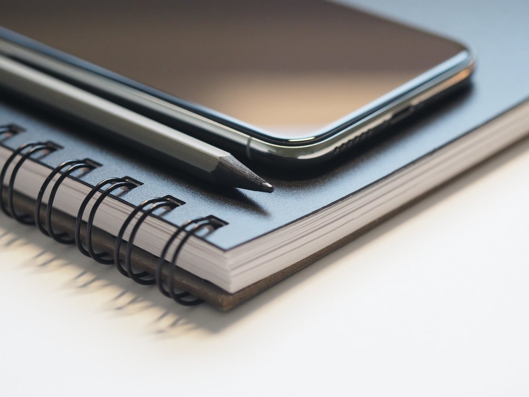 closeup photo of black smartphone near black and grey pencil on black spiral notebook | How To Maintain Your Blogging Routine
