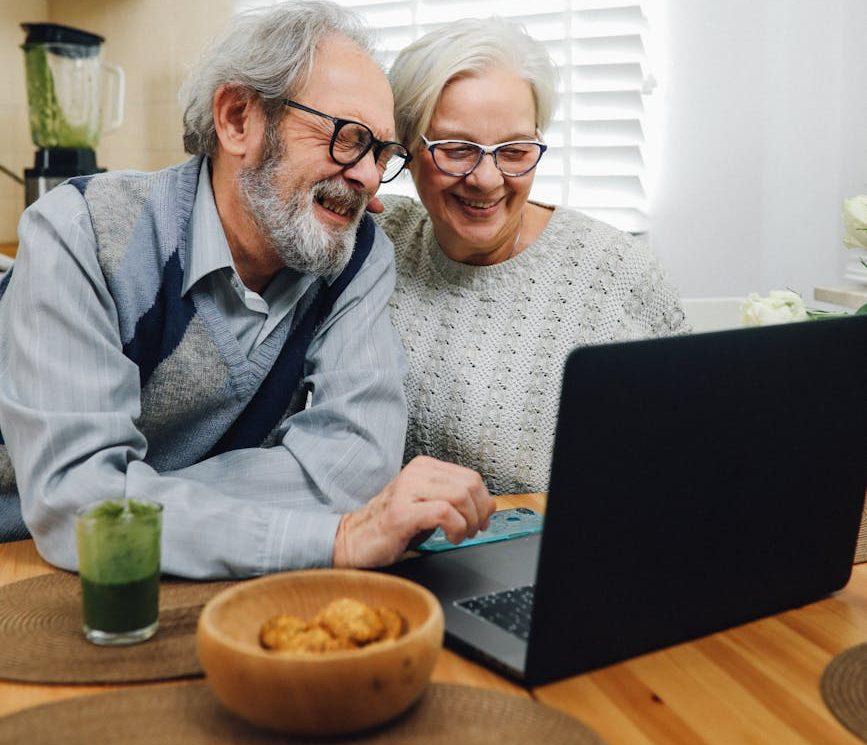 senior couple smiling and using a laptop | The Challenges And Advantages Of Online Dating As A Mature Adult